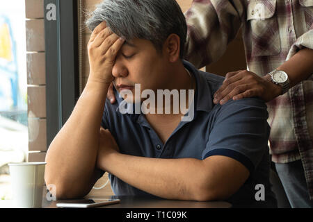 Middle-aged Asian man 40 years old, stressed and tired, are sitting in fast food restaurant and have friends standing behind to encourage. Concept of  Stock Photo