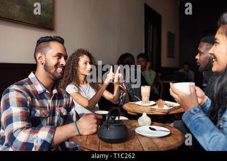 Smiling friends drinking coffee while sitting together in a cafe Stock Photo