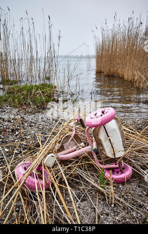 Old pink kids tricycle discarded at a river bank, environment pollution or a crime concept picture. Stock Photo