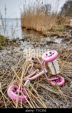 Old kids tricycle discarded at a river bank, environment pollution or a crime scene concept picture. Stock Photo