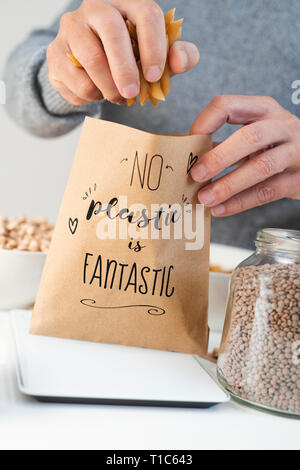 closeup of a caucasian man putting some dry macaroni on a brown paper bag, with the text no plastic is fantastic written in it, placed on an electroni Stock Photo