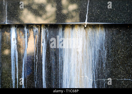 Black Polished Granite Wall with White Outgrowths Leaking from the Weather. Streaks on the Wall Stock Photo