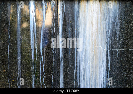 Black Polished Granite Wall with White Outgrowths Leaking from the Weather. Streaks on the Wall Stock Photo