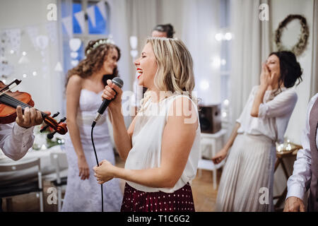 A young woman singing on a wedding reception, bride and guests dancing. Stock Photo