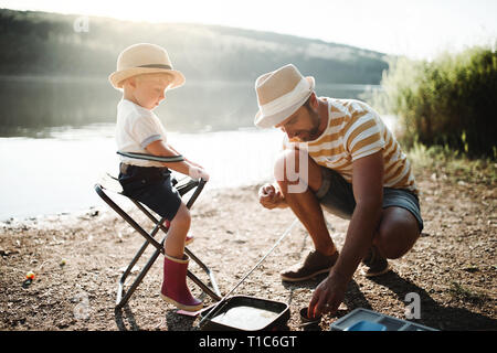 A mature father with a small toddler son outdoors fishing by a lake, talking. Stock Photo