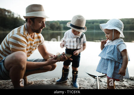 A mature father with small toddler children fishing by a lake, holding a fish. Stock Photo