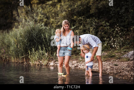 Young family with two toddler children outdoors by the river in summer, playing.
