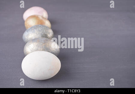 Row of colorfully nacreous Easter eggs on black wooden background Stock Photo