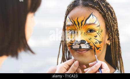 Little girl getting her face painted by face painting artist. Stock Photo