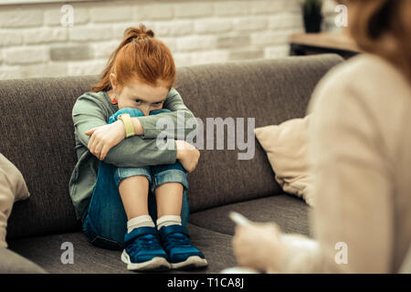 Depressed cute cheerless girl hugging her legs Stock Photo