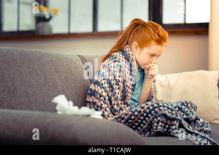 Unhappy red haired girl coughing in her hand Stock Photo