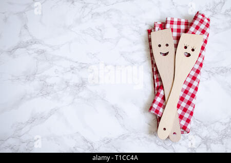 Kitchen wooden utensils with smile on red checkered napkin on marble background. Wooden spoons with male and female faces. Family cooking concept. Rom Stock Photo