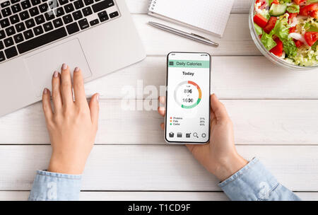Female hands using smartphone and eating fresh salad Stock Photo