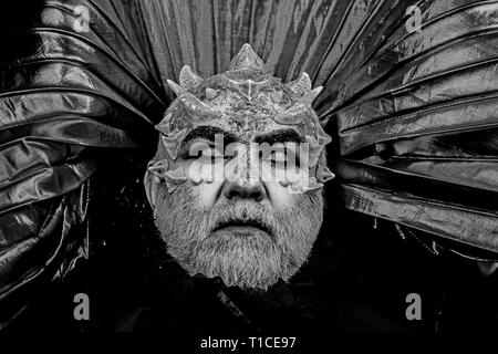 Man with thorns or warts, face covered with glitters. Demon with golden collar on black background. Fantasy concept. Senior man with white beard Stock Photo