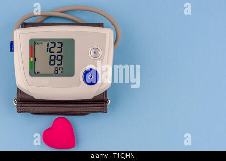 Modern electronic blood pressure monitor with red heart on a blue background. Stock Photo
