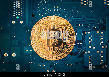 Mining Bitcoin concept - gold coin on a blue printed circuit board - PCB Stock Photo