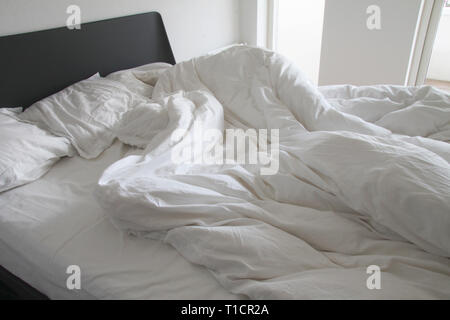 Messy white bedding sheets and pillows with wrinkles on bed  in a white bedroom Stock Photo