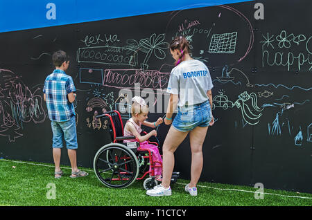 Dnipro, Ukraine - June 27, 2018: Volunteers with children draws scrawl chalk on a blackboard in inclusive gaming park of the city Stock Photo