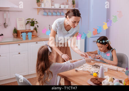 Positive delighted female person helping her daughters Stock Photo