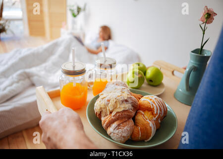Husband making surprise bringing breakfast and flowers for wife Stock Photo