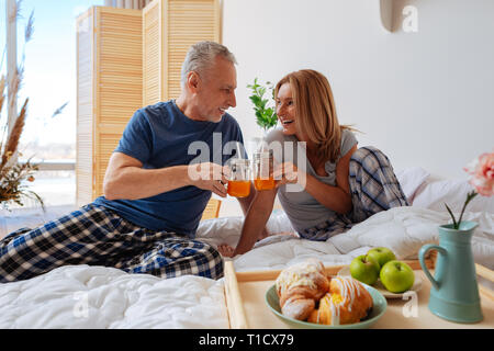 Couple clanging glasses with juice having breakfast in bed Stock Photo