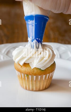 Piping white frosting onto mini cupcake. Stock Photo