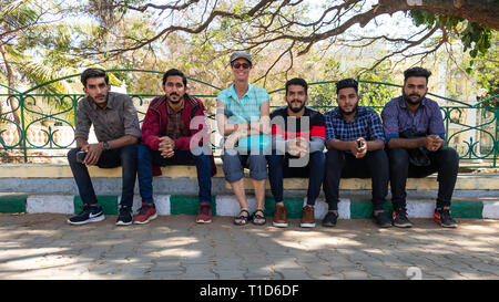 Female tourist with five young Indian men sitting on the sidewalk Stock Photo