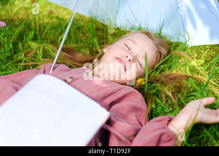 little girl fell asleep with a book in the park on the grass on the lawn Stock Photo