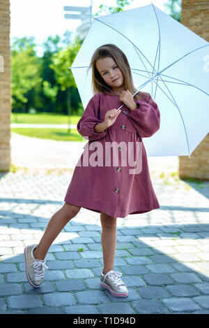 pretty little girl in burgundy dress with white umbrella on sunny day. concept of fashion Stock Photo