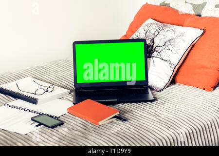 Green screen laptop, notebook, smartphone, glasses and pen on bad, education concept background. Stock Photo