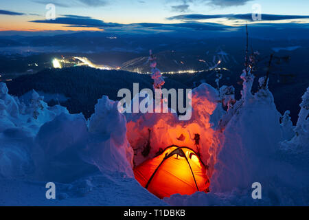 tourist tent in the winter in the mountains, illuminated by a lantern, sunset Stock Photo