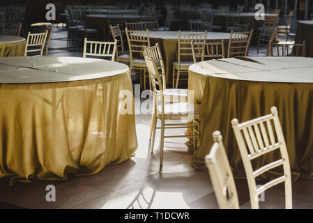 Round tables with tablecloths, empty, surrounded by wooden chairs, in a restaurant. Stock Photo