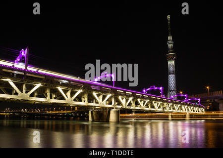 The Tobu railway line running over the Sumida River in downtown Tokyo is lit up in vibrant purple lights. Above, the Skytree is also lit up and a long Stock Photo