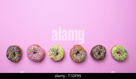 Donuts assorted. Doughnuts with colorful sprinkles and icing on pink background, top view, copy space Stock Photo