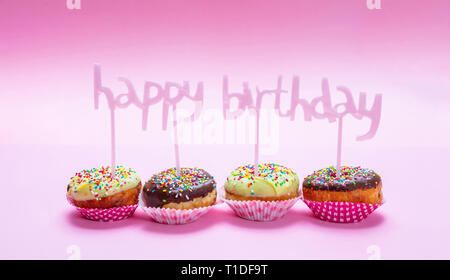 Happy birthday. Mini cakes with icing and colorful sprinkles on pink background, text happy birthday decoration Stock Photo