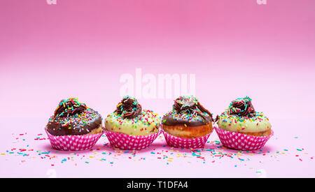 Cupcakes on pink. Mini cakes with icing and colorful sprinkles on pink background, closeup view Stock Photo