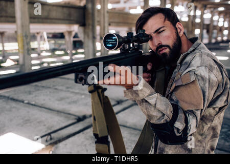 Concentrated and professional shooter is taking aim. He is looking through special lens. The rifle is just regular machine for playing paintball game. Stock Photo
