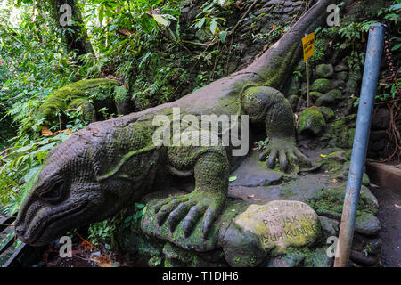 A stone statue of the Komodo monitor, covered with moss and lichen in a tropical green forest near the river. Giant Lizard in Sacred Monkey Forest, Ub Stock Photo