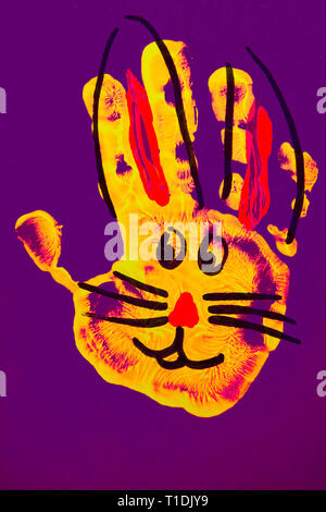 Easter bunny from yellow red kids hand imprint on purple background upright Stock Photo
