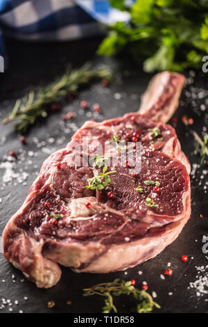 Raw beef tomahawk steak with salt pepper and rosemary on slate plate. Stock Photo