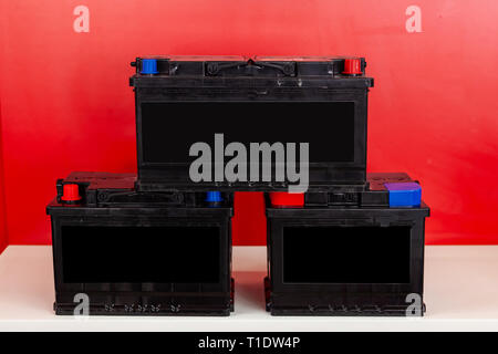 Three new black rechargeable batteries stand pyramid on each other on a red background with white inscriptions. Auto service industry.	 Stock Photo