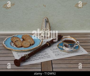 English teacup with saucer and a cake plate with cookies, fine bone china porcelain, metronome for music and a block flute on a sheet of music Stock Photo