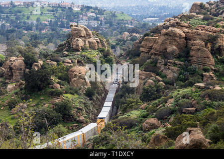 Los Angeles, California, USA - March 20, 2019:  Freight train passing rock formations and expensive San Fernando Valley homes in the Santa Susana Pass