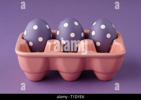 Pink ceramic egg tray with purple painted Easter eggs with dots on purple background, holiday concept Stock Photo