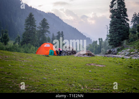 A person entering an Orange coloured tent set up for camping in the Himalayan region of Kashmir Stock Photo
