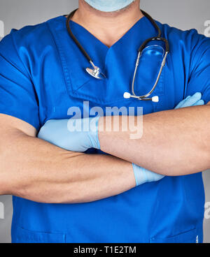 doctor in blue uniform and latex gloves crossed his arms over his chest, a stethoscope hanging on his neck Stock Photo