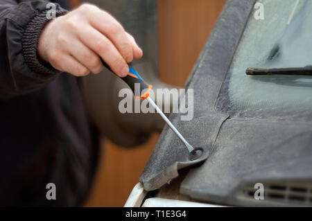 Human hand, holding a screwdriver, fixing a damaged plastic cover of a vehicle bonnet. Selective focus closeup Stock Photo
