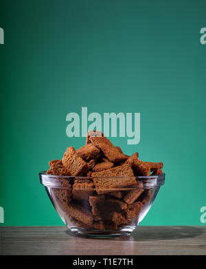 Rye crackers with spices and salt in transparent plate on green background Stock Photo