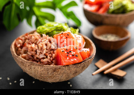 Poke bowl with raw salmon fish, chuka salad and rice in coconut bowls on black background Stock Photo