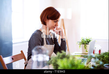Young creative woman in a flower shop, using laptop. A startup of florist business. Stock Photo